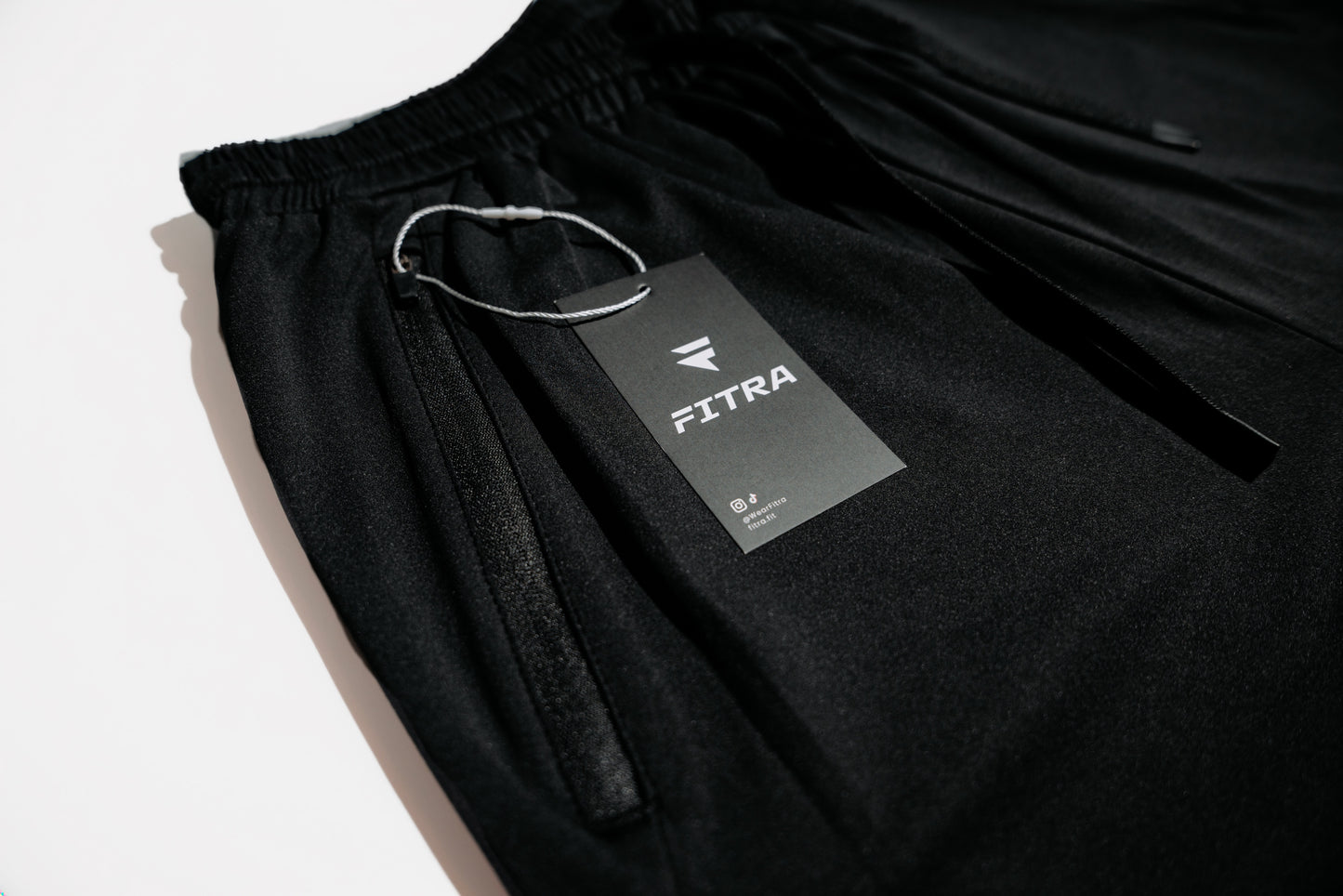 Fitra branded hang tag resting on the elastic waistband of the black Core Short