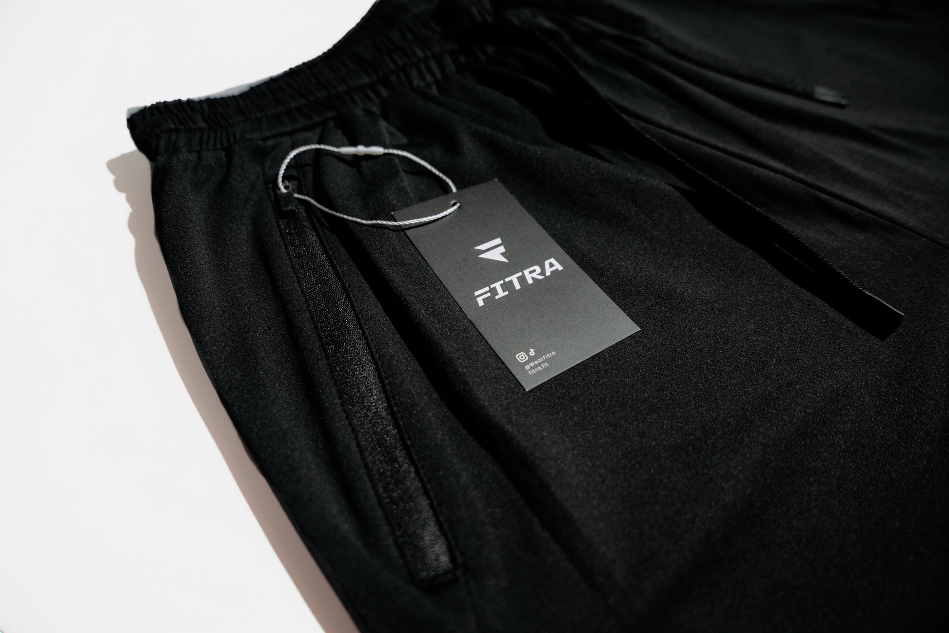 Fitra branded hang tag resting on the elastic waistband of the black Core Short